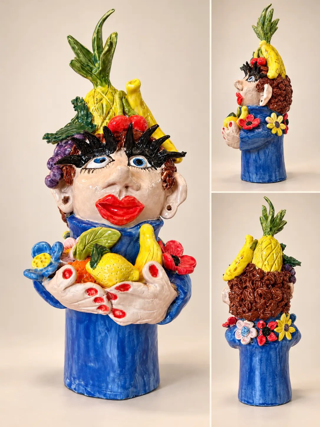 Personnage en céramique bleue coiffé de fruits et entouré de fleurs colorées.